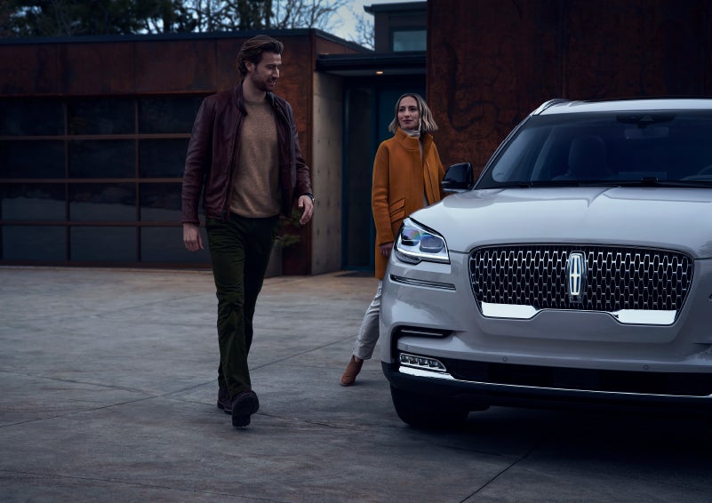 A man and a woman approaching a 2024 Lincoln Aviator® SUV, which illuminates certain lights when they are close | Jenkins & Wynne Lincoln in Clarksville TN